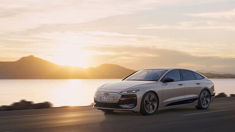 Audi A6 e-tron drives on a riverside road with the evening sun in the backdrop