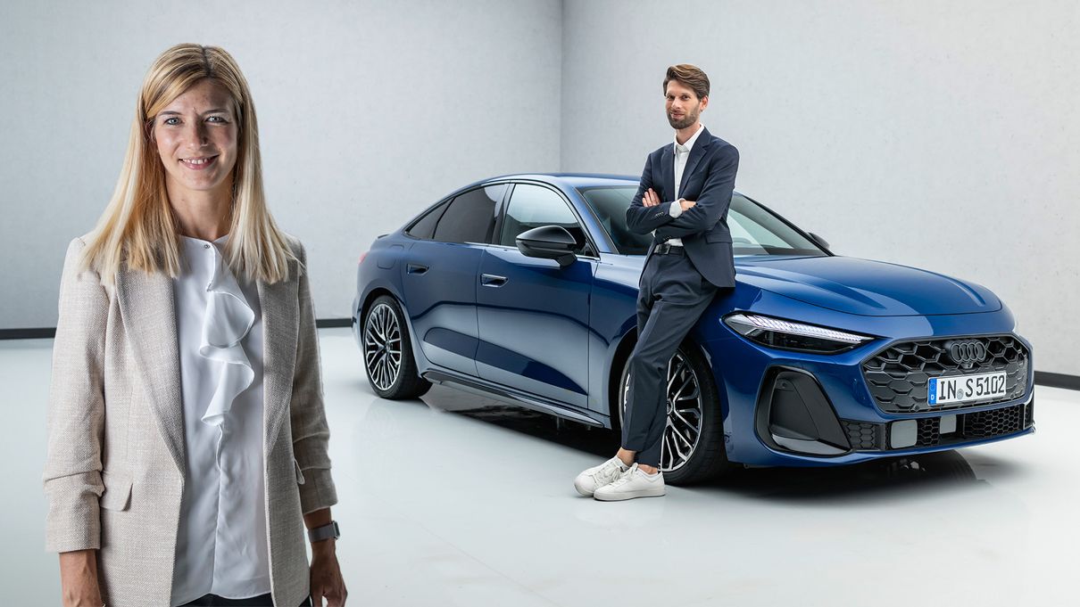 Luisa Werther steht im Vordergrund, im Hintergrund lehnt Jakob Hirzel an einem blau lackierten Audi A5