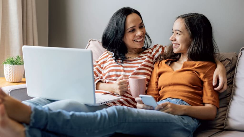 Eine Frau und ein Mädchen sitzen auf einer Couch und haben einen Laptop auf dem Schoß