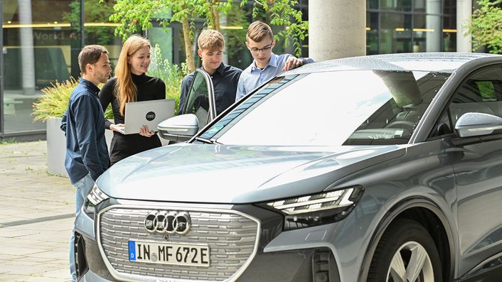 Vier Mitarbeitende von Audi sind im Gespräch und stehen hinter einem Audi