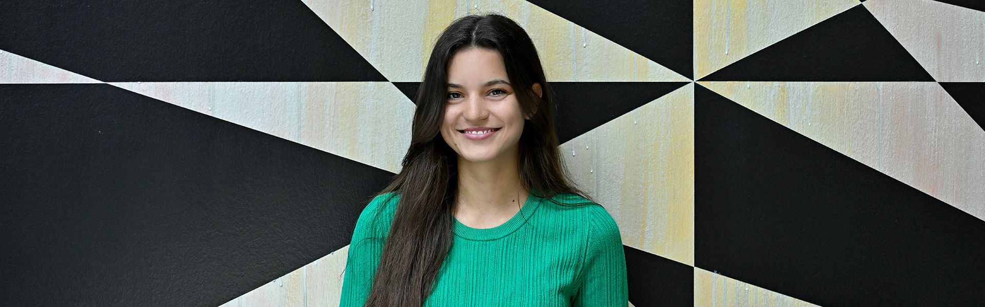 Thais is standing in front of a wall and smiles into the camera