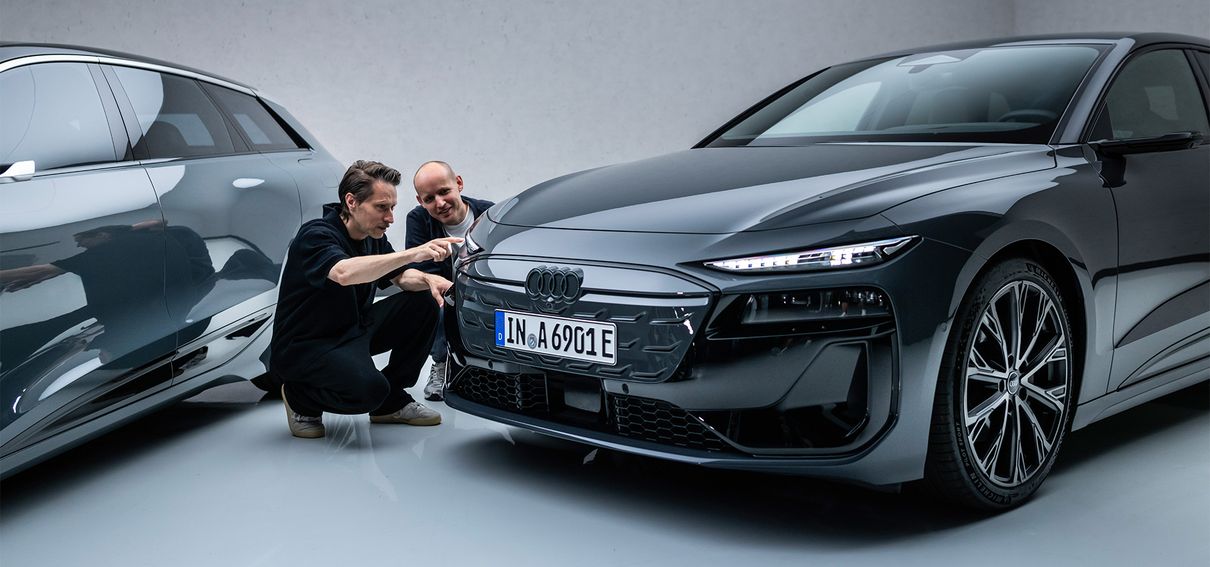 Sascha Heyde and Wolf Seebers kneel next to an Audi A6 e-tron model and talk about the lights