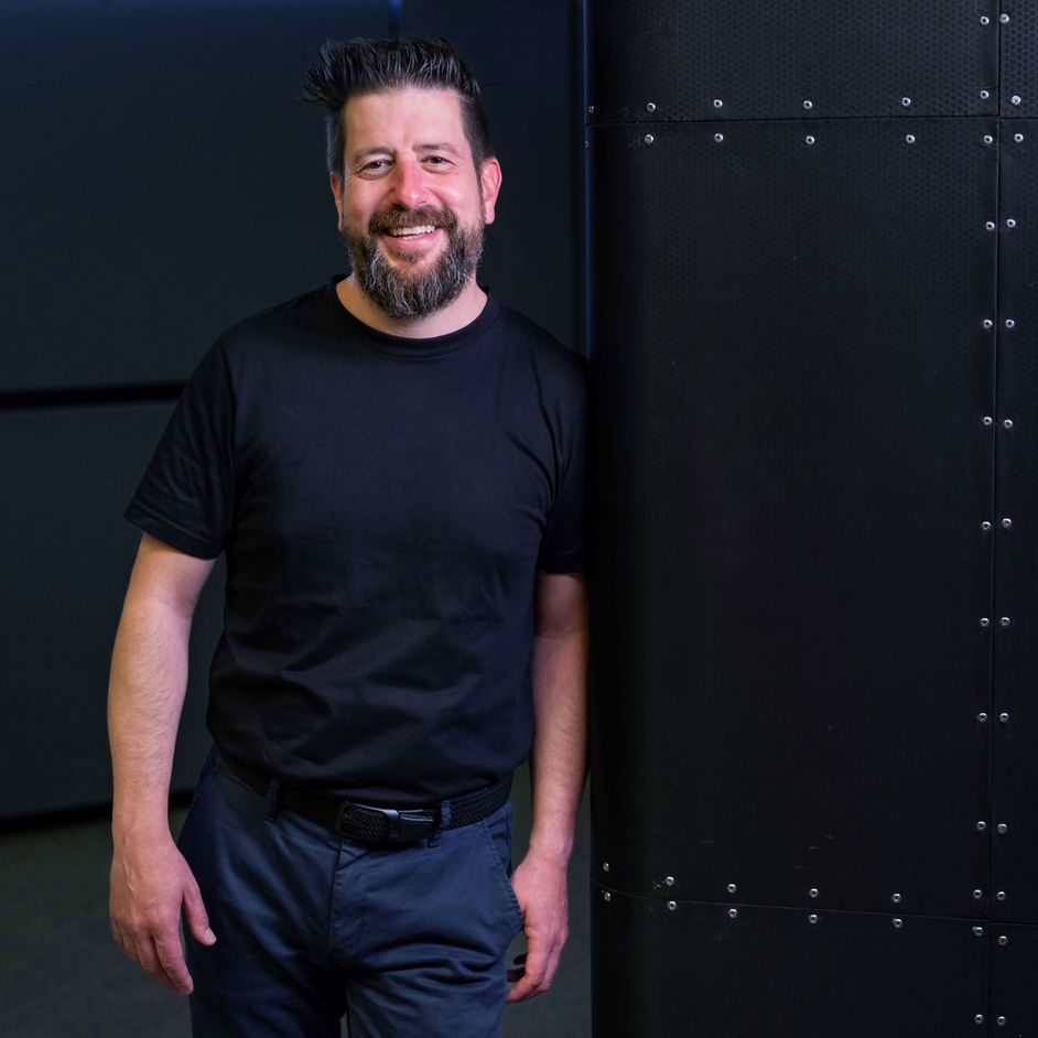 Portrait of Andreas Valencia Pollex leaning against a black wall smiling