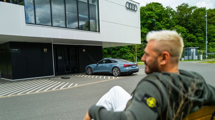 Jasko sitzt auf einer Bank vor dem Audi charging hub während sein Auto auflädt