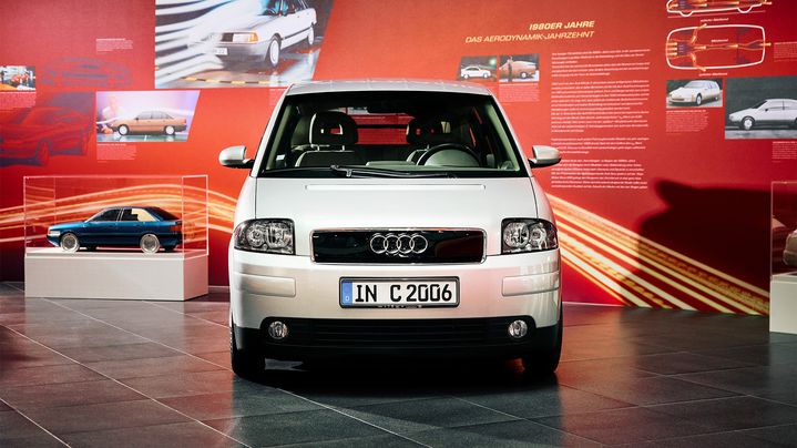 An older Audi model is on display in front of a billboard